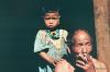 <p>Damro Village, Upper Siang, Arunachal Pradesh.  December, 1994<br />
A Wills Navy Cut cigarette was enough exotic pleasure for this village chief (known as a gaon-bura) to permit camping in the vicinity of his village.  Grand daughter Pema looks on inquisitively.</p>

